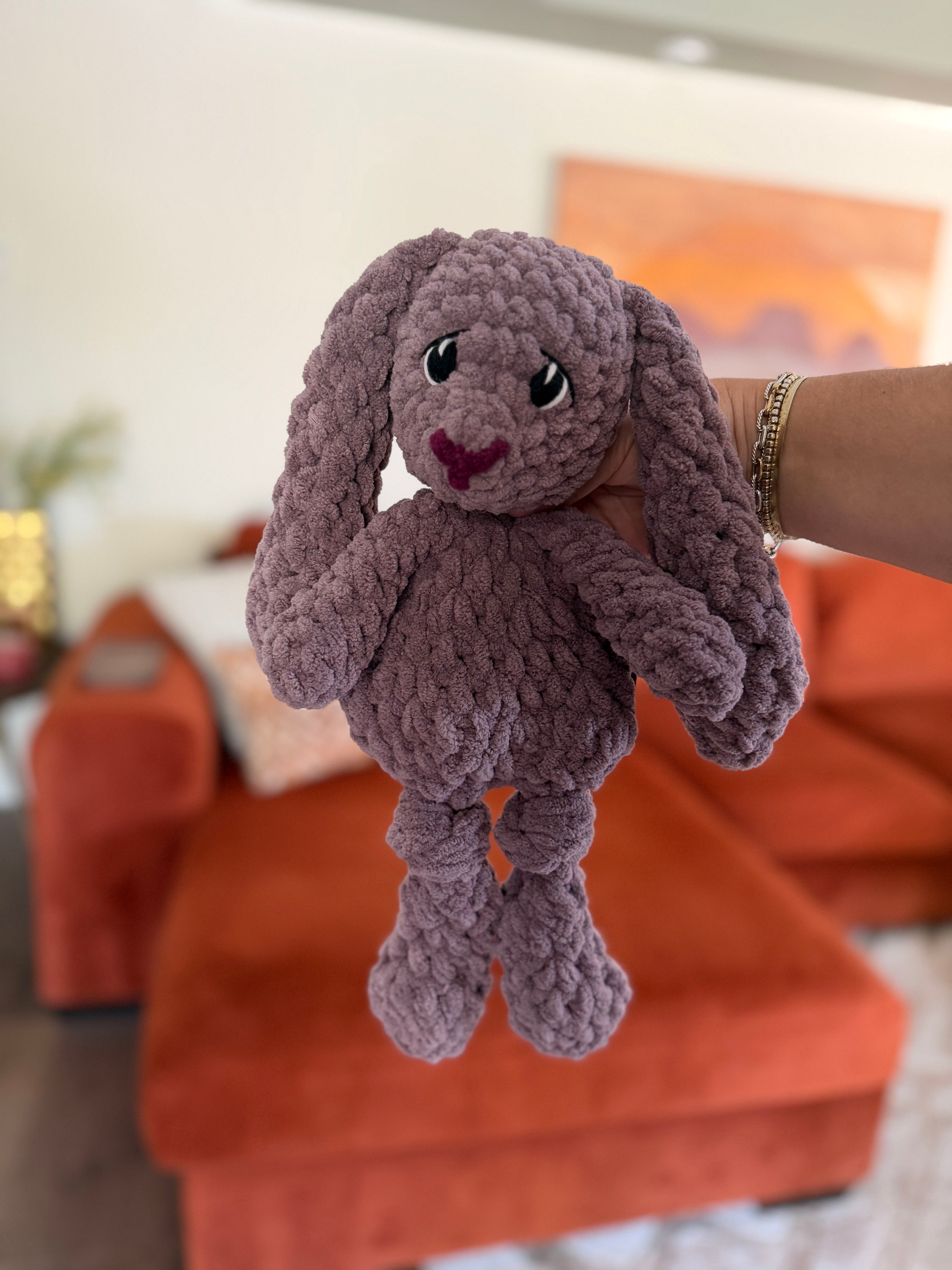 Lavender purple crochet bunny in front of blurred orange couch