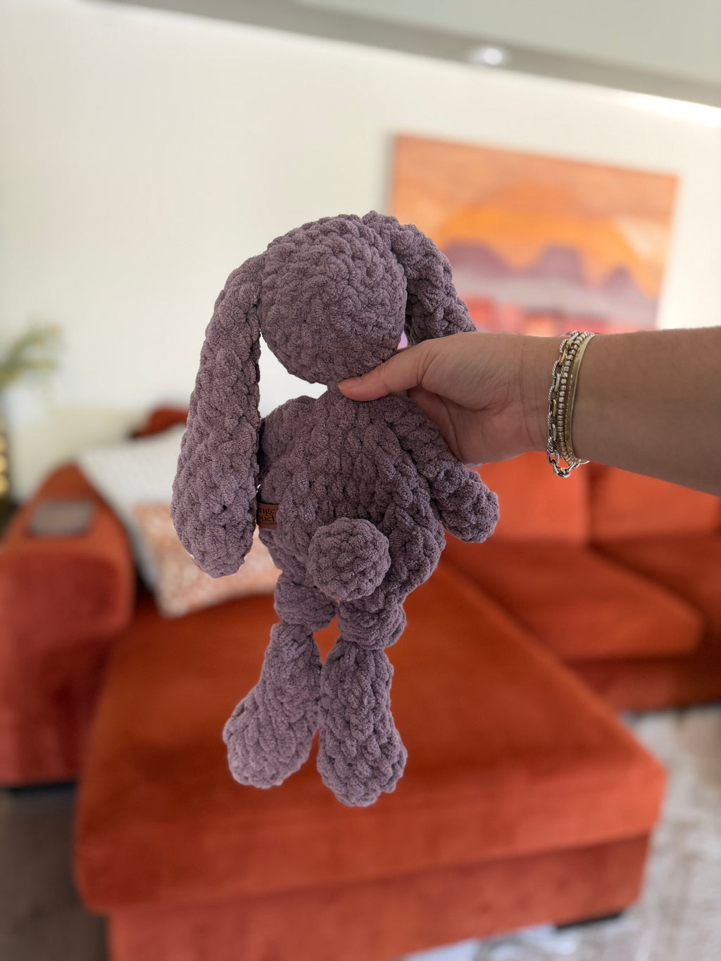 Lavender purple crochet bunny in front of blurred orange couch