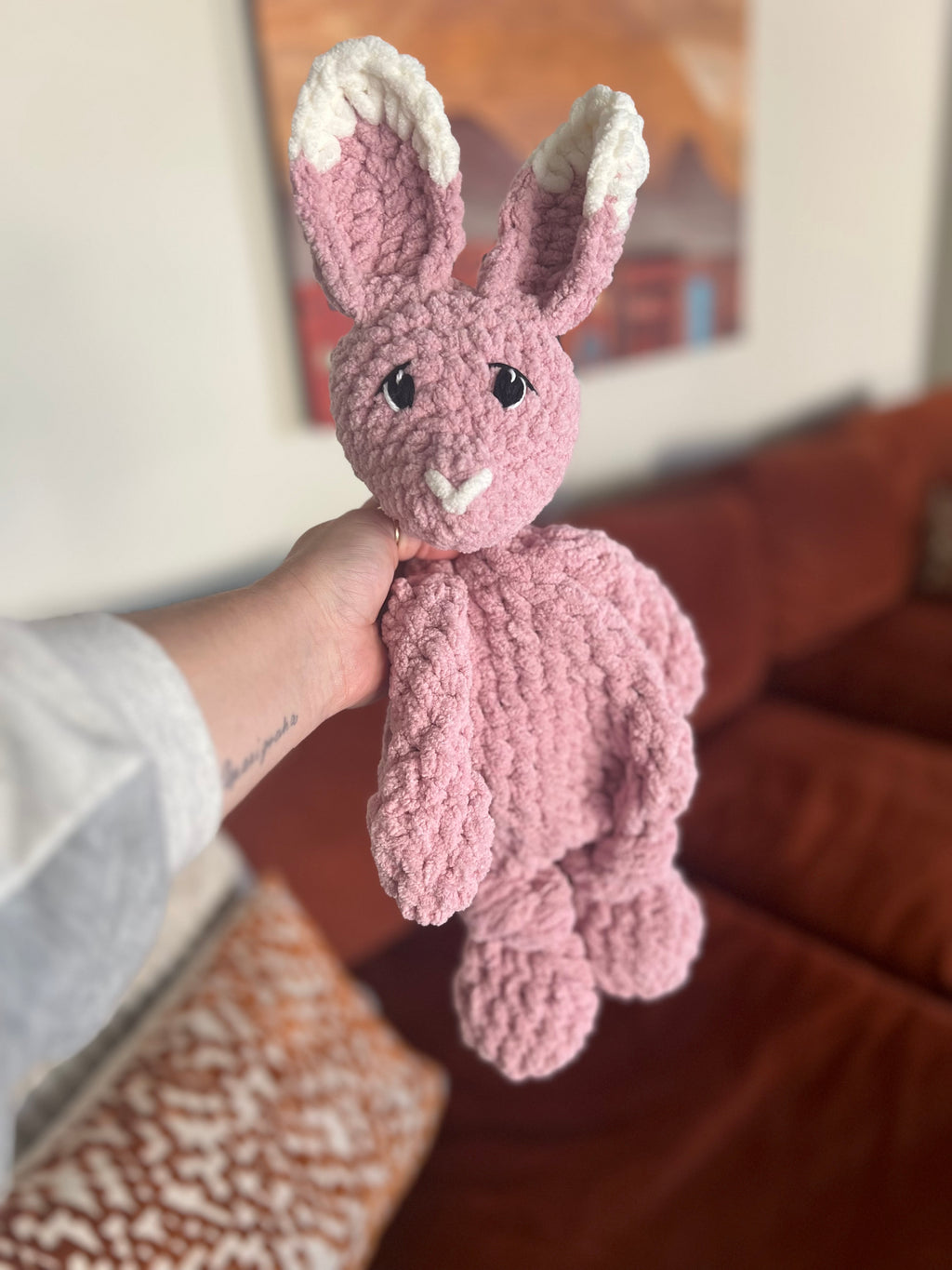pink and white crochet bunny in front of blurred orange couch