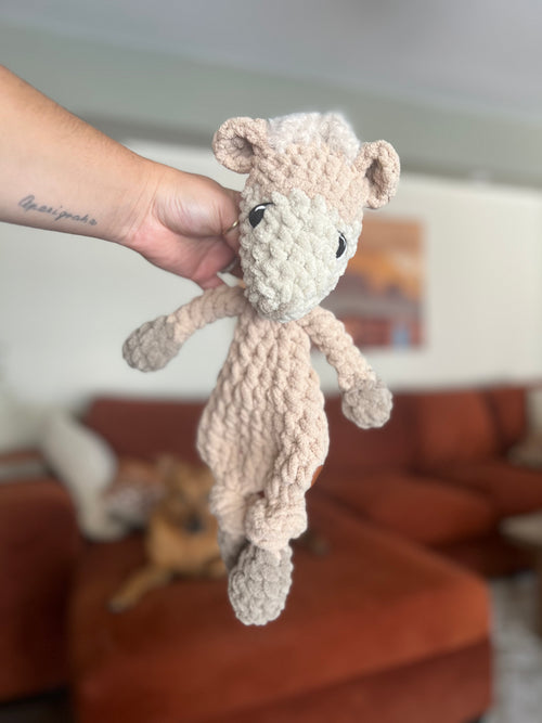 Hand holding a beige crochet alpaca in a home setting