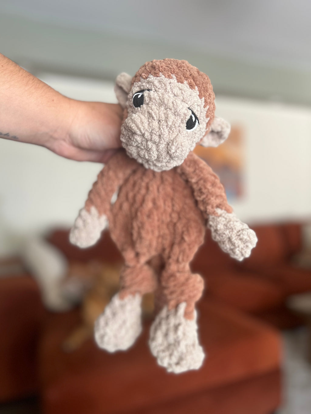 crochet brown and beige monkey in front of blurred orange couch