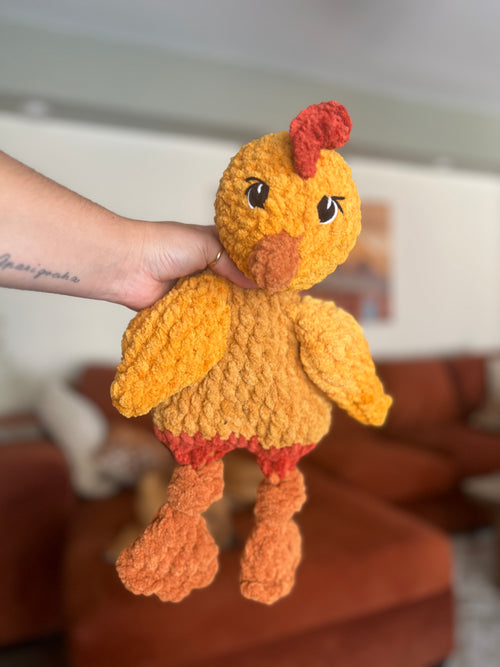 Hand holding a small crochet chicken toy against a blurred indoor background