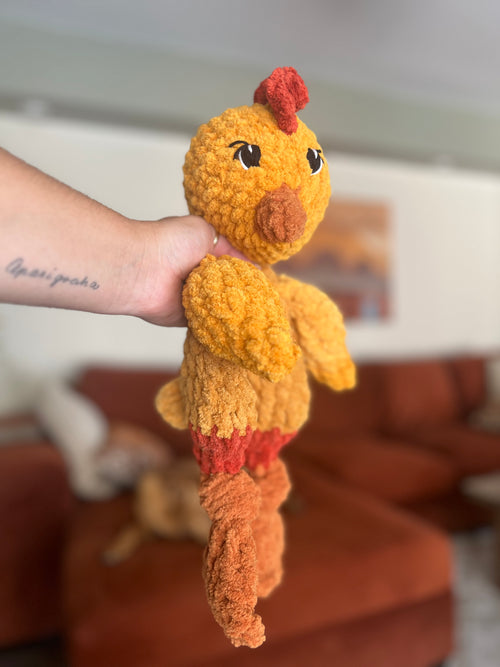 Hand holding a small crochet chicken toy against a blurred indoor background