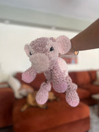 Pink plush cow toy held by a hand against a blurred indoor background