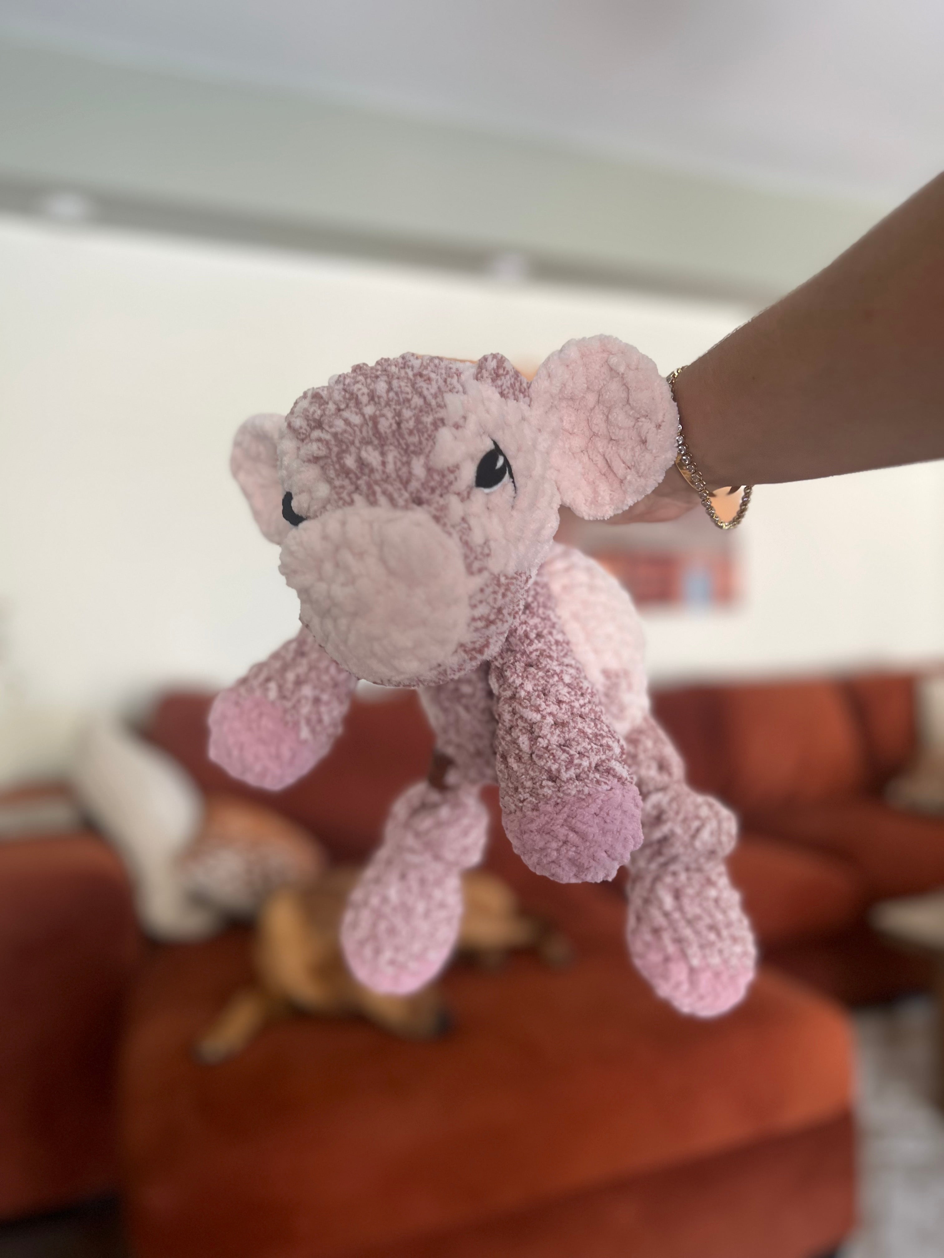 Pink plush cow toy held by a hand against a blurred indoor background