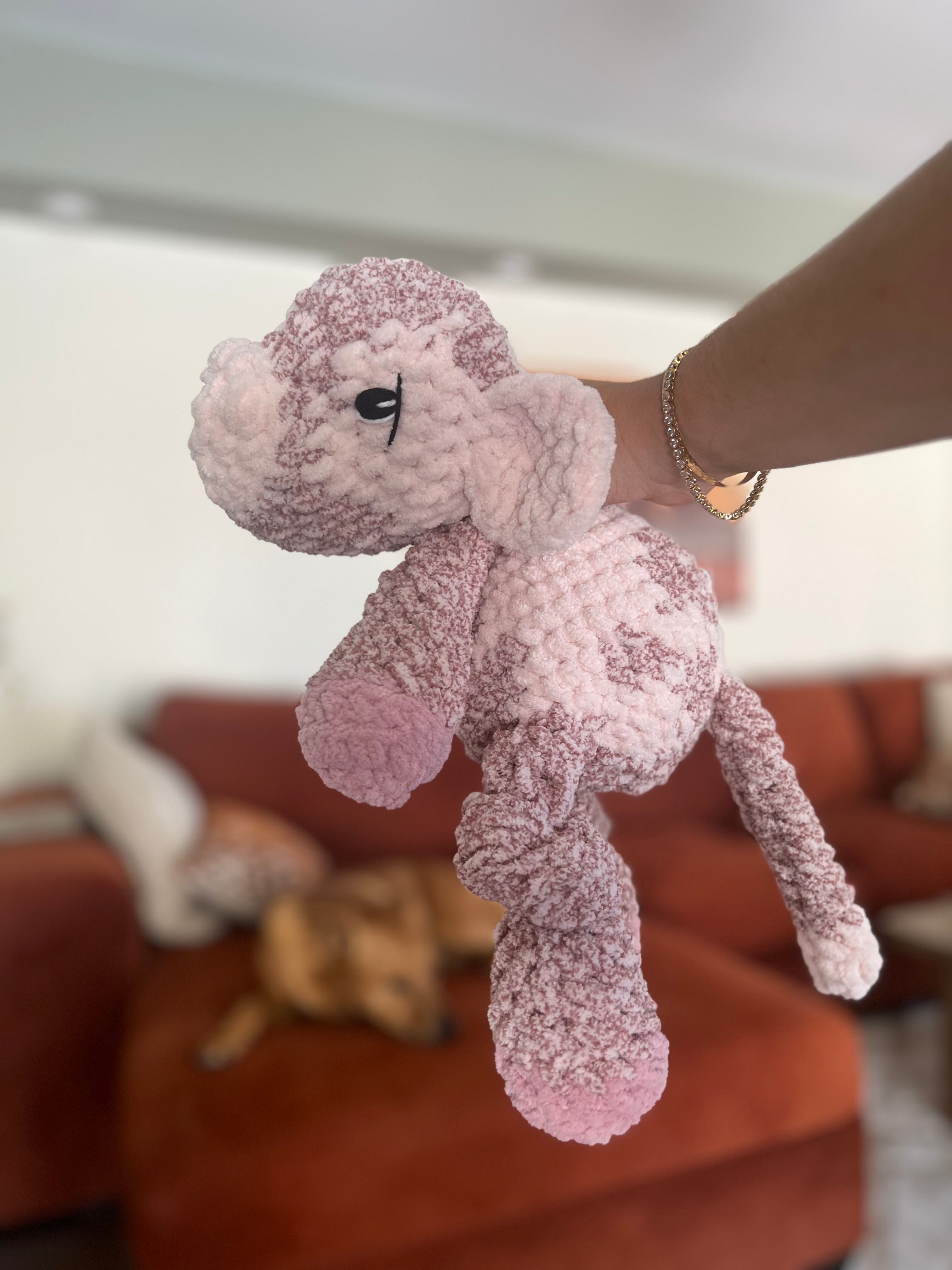 Pink plush cow toy held in front of a blurred indoor background