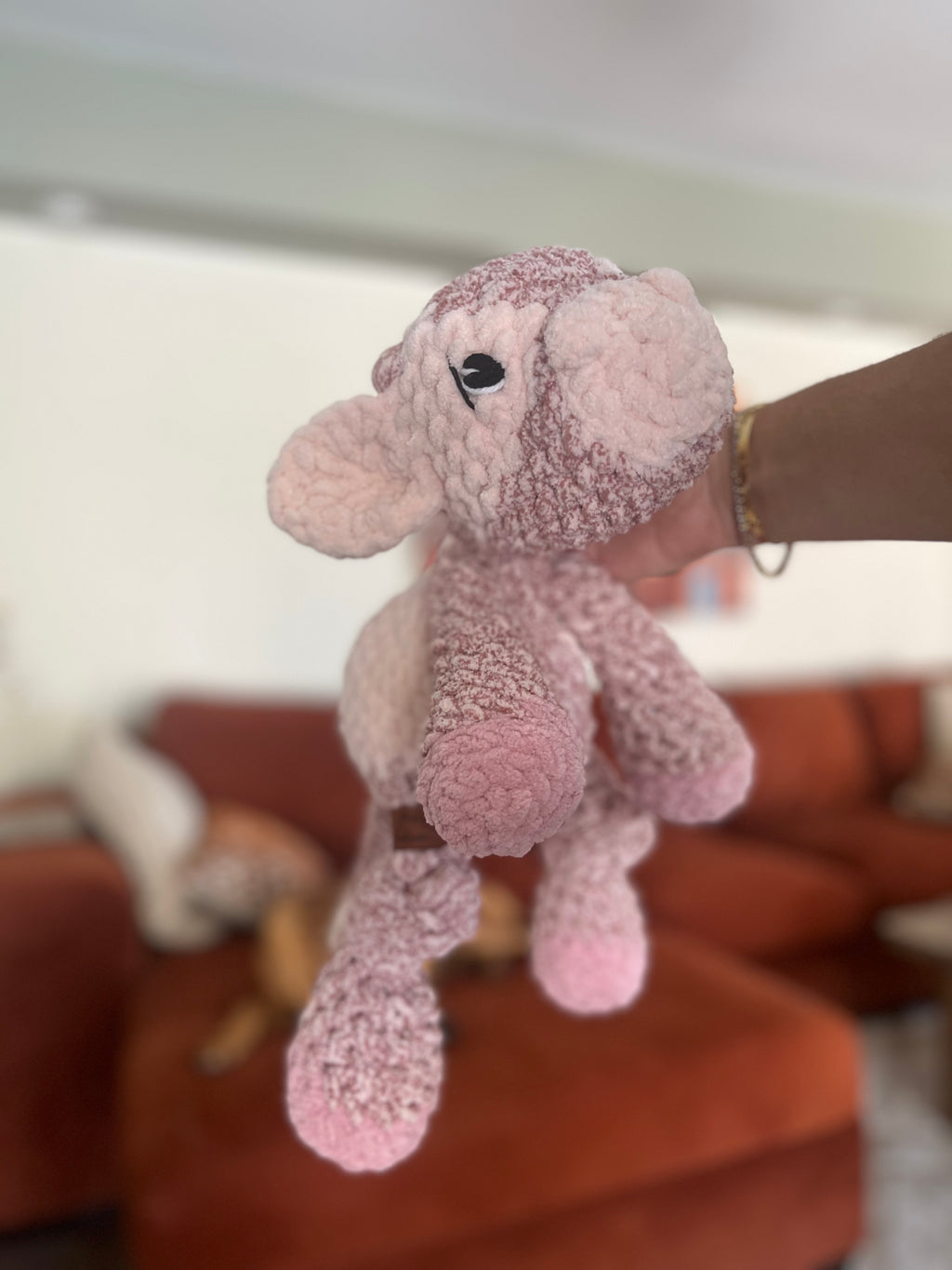 Pink plush cow toy held by a hand with a blurred background