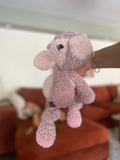 Pink plush cow toy held by a hand with a blurred background