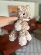 Crocheted light tan fox held by a hand with a blurred background