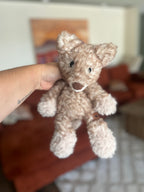 Crocheted light tan fox held by a hand with a blurred background