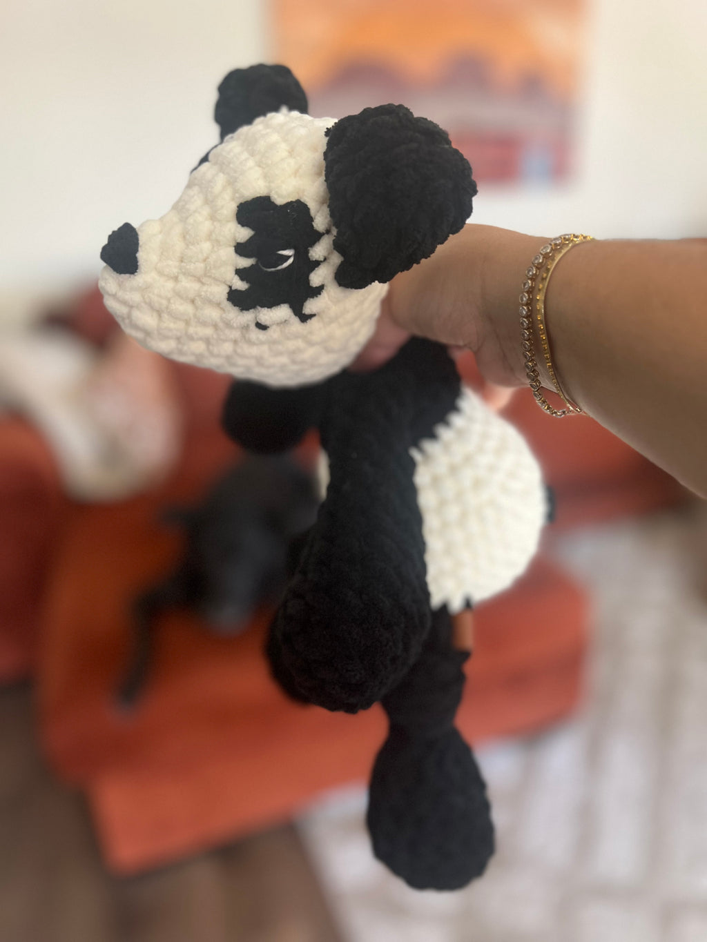 Crochet black and white panda bear in front of blurred orange couch