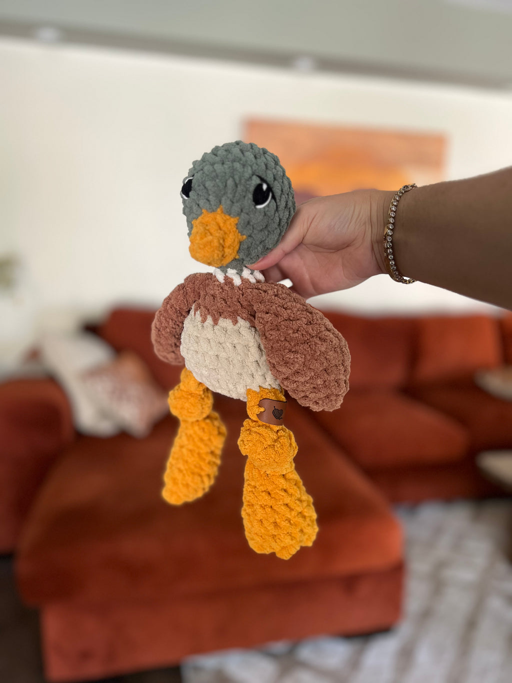 green, yellow, beige, and brown mallard duck crochet plushie in front of blurred orange couch