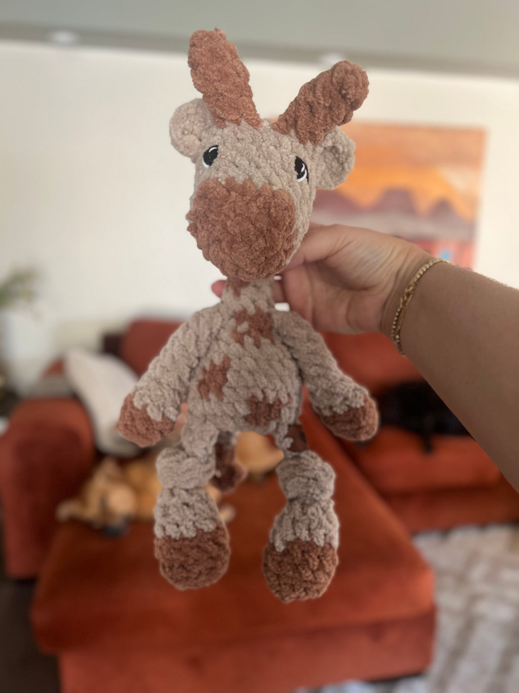 Hand holding small crochet giraffe plushie with blurred background