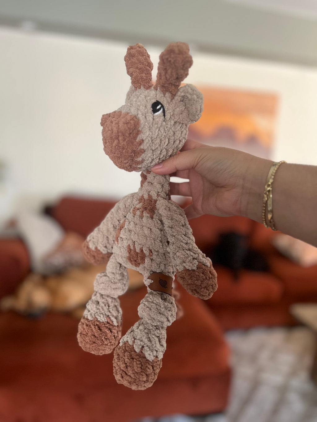 Hand holding small crochet giraffe plushie with blurred background