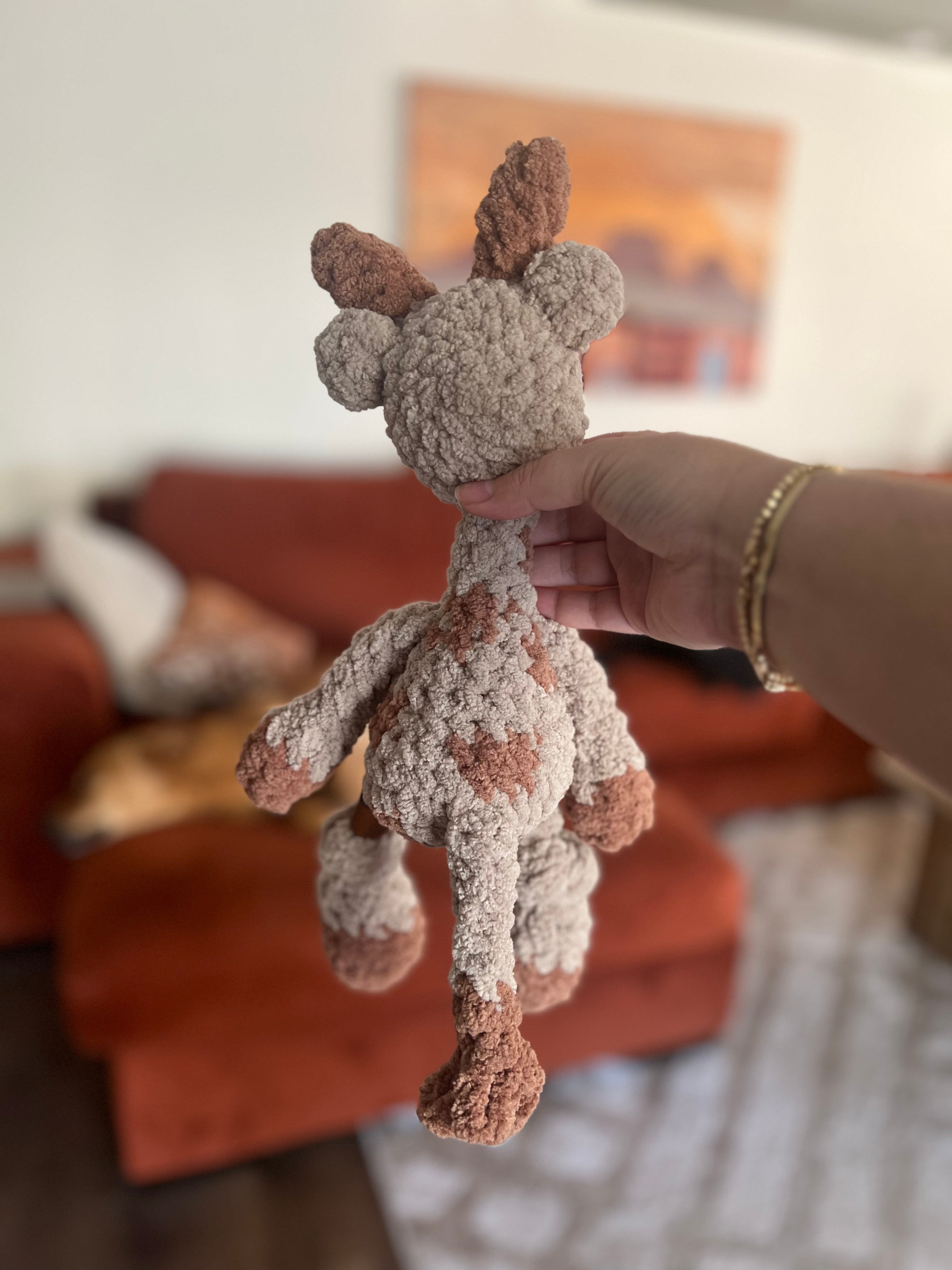 Hand holding small crochet giraffe plushie with blurred background