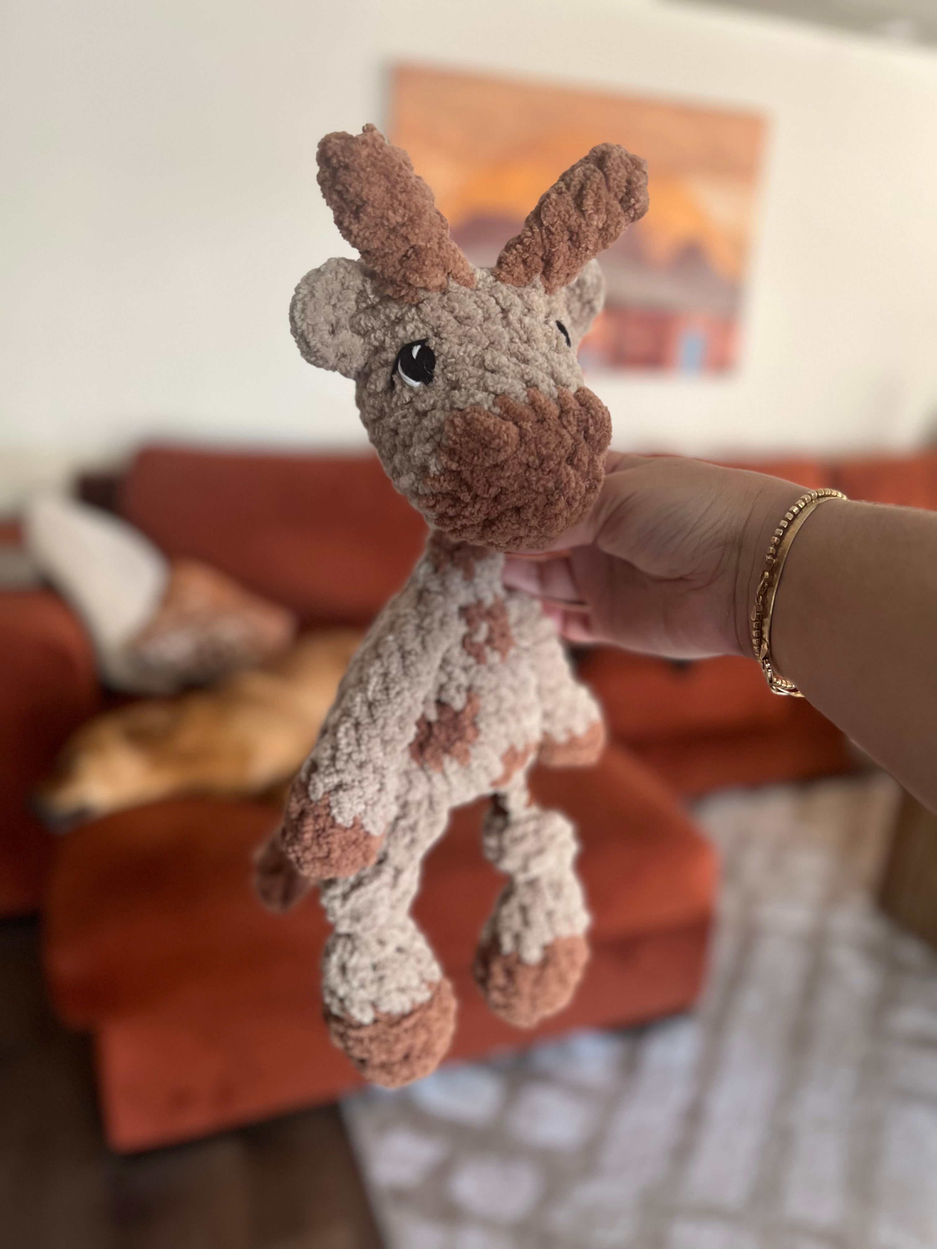 Hand holding small crochet giraffe plushie with blurred background
