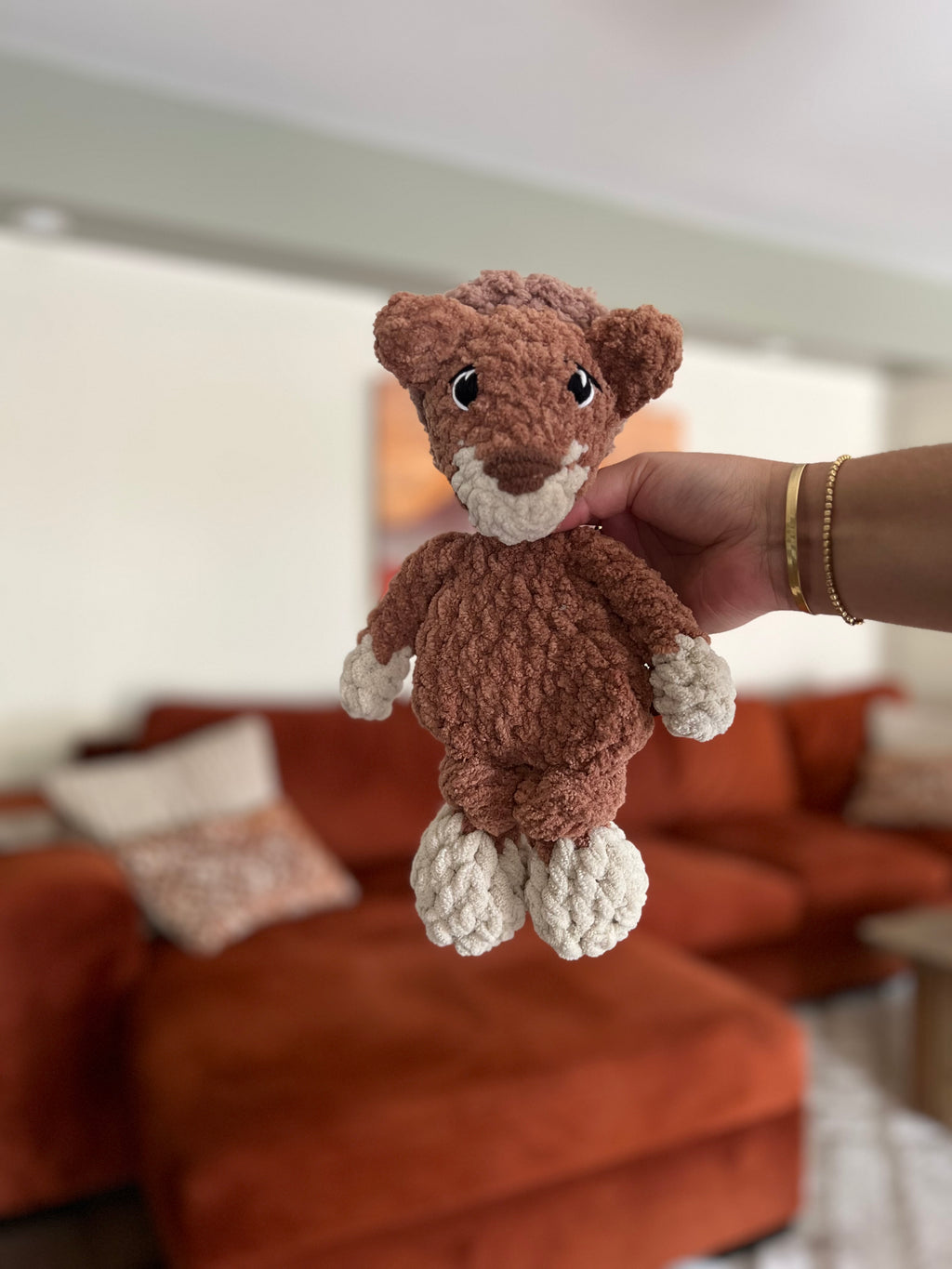 brown and beige crochet lion in front of blurred orange couch