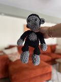 Hand holding a small crocheted gorilla toy in a living room setting.