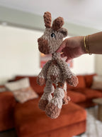 beige and brown crochet giraffe in front of orange blurred couch