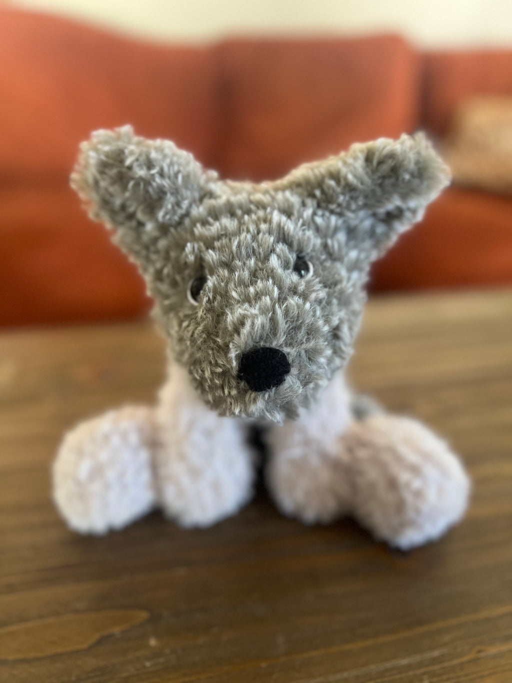 Crochet plush toy grey dog on a wooden surface with a blurred background