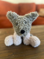 Crochet plush toy grey dog on a wooden surface with a blurred background