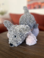 Crochet plush toy grey dog on a wooden surface with a blurred background