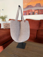 Beige crochet tote bag on a stand in front of a orange couch with a painting in the background