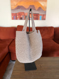 Beige crochet tote bag on a stand in front of a orange couch with a painting in the background