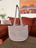 Crochet beige tote bag on a wooden surface with a blurred living room background