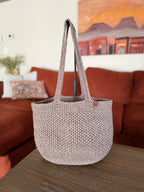 Crochet beige tote bag on a wooden surface with a blurred living room background