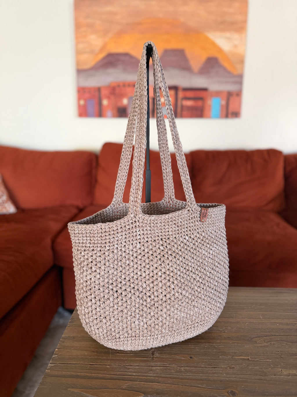 Crochet beige tote bag on a wooden surface with a blurred living room background