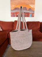 Crochet beige tote bag on a wooden surface with a blurred living room background