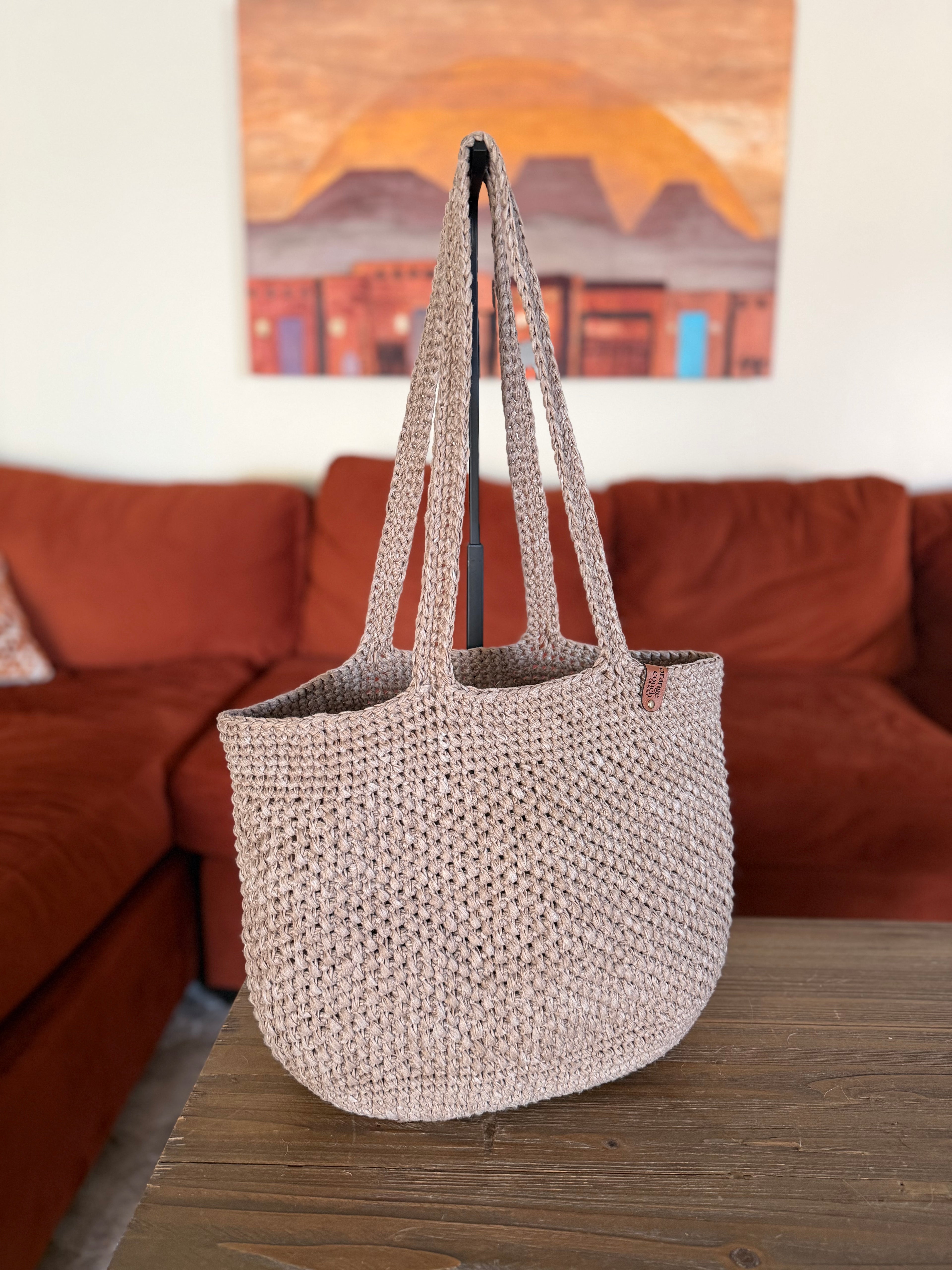 Crochet beige tote bag on a wooden surface with a blurred living room background