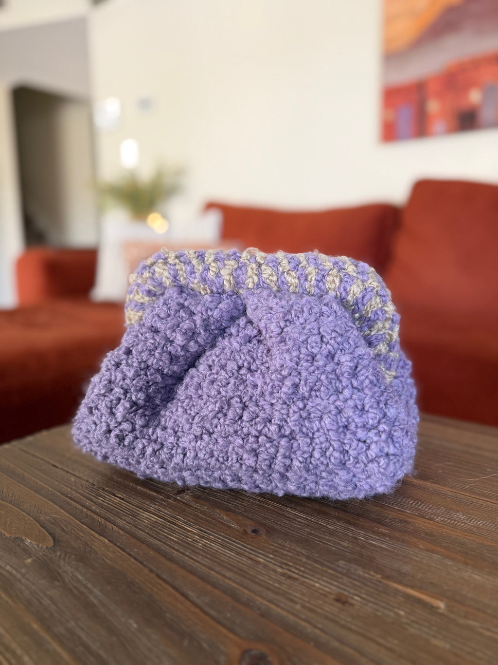 Purple crochet clutch with beige striped handle in front of blurred orange couch