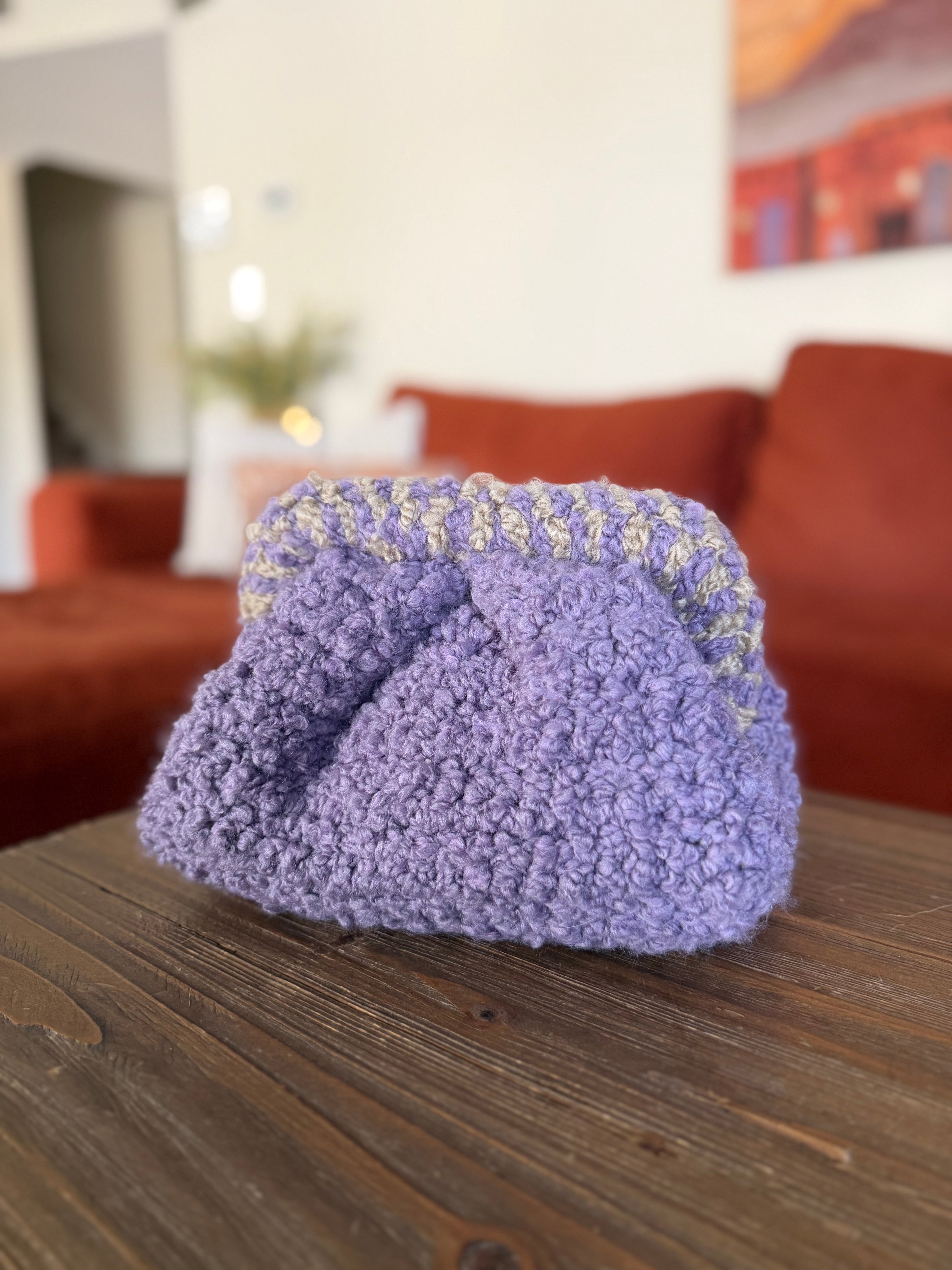 Purple crochet clutch with beige striped handle in front of blurred orange couch