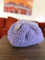 Purple crochet clutch with beige striped handle in front of blurred orange couch