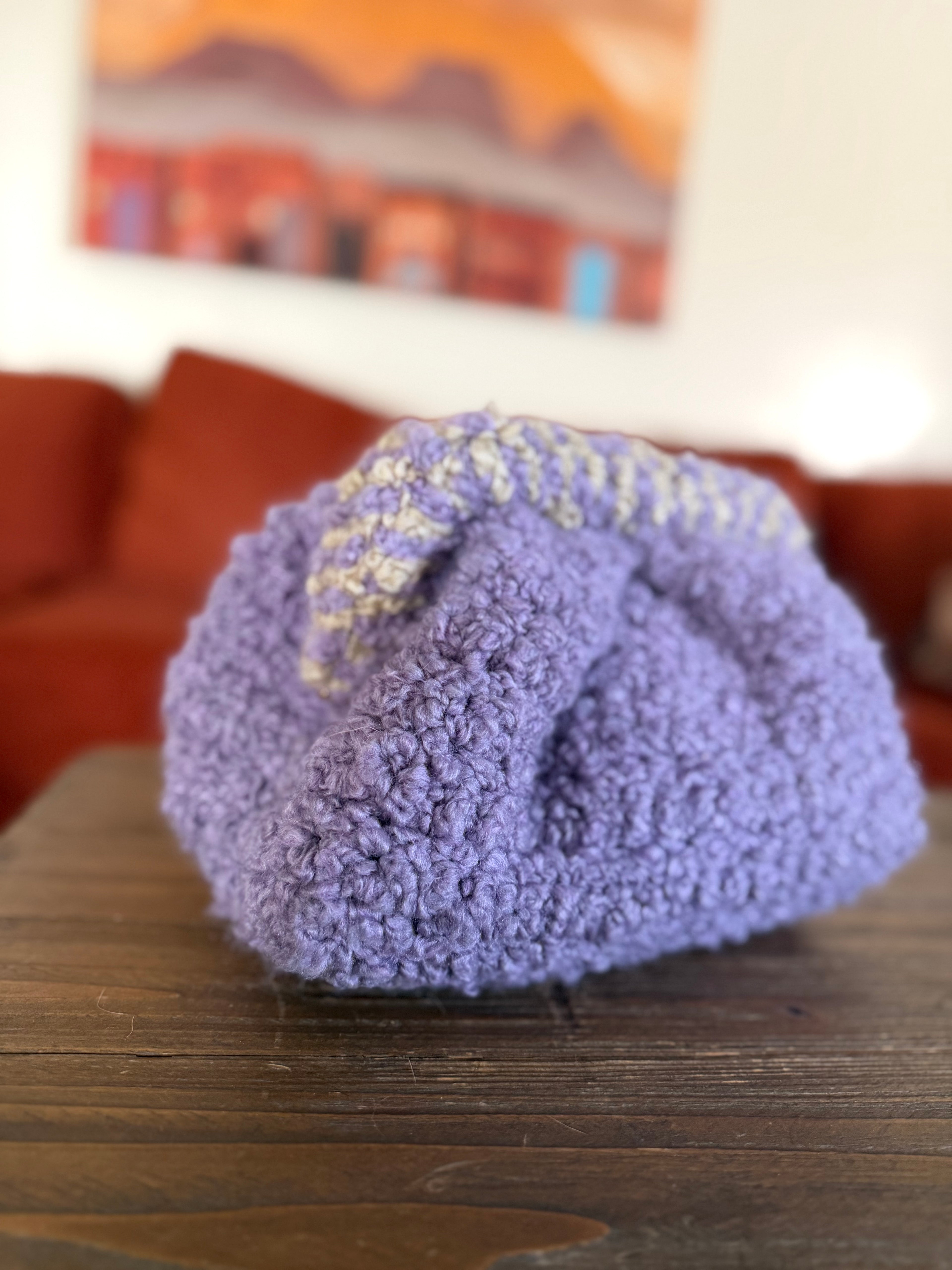 Purple crochet clutch with beige striped handle in front of blurred orange couch