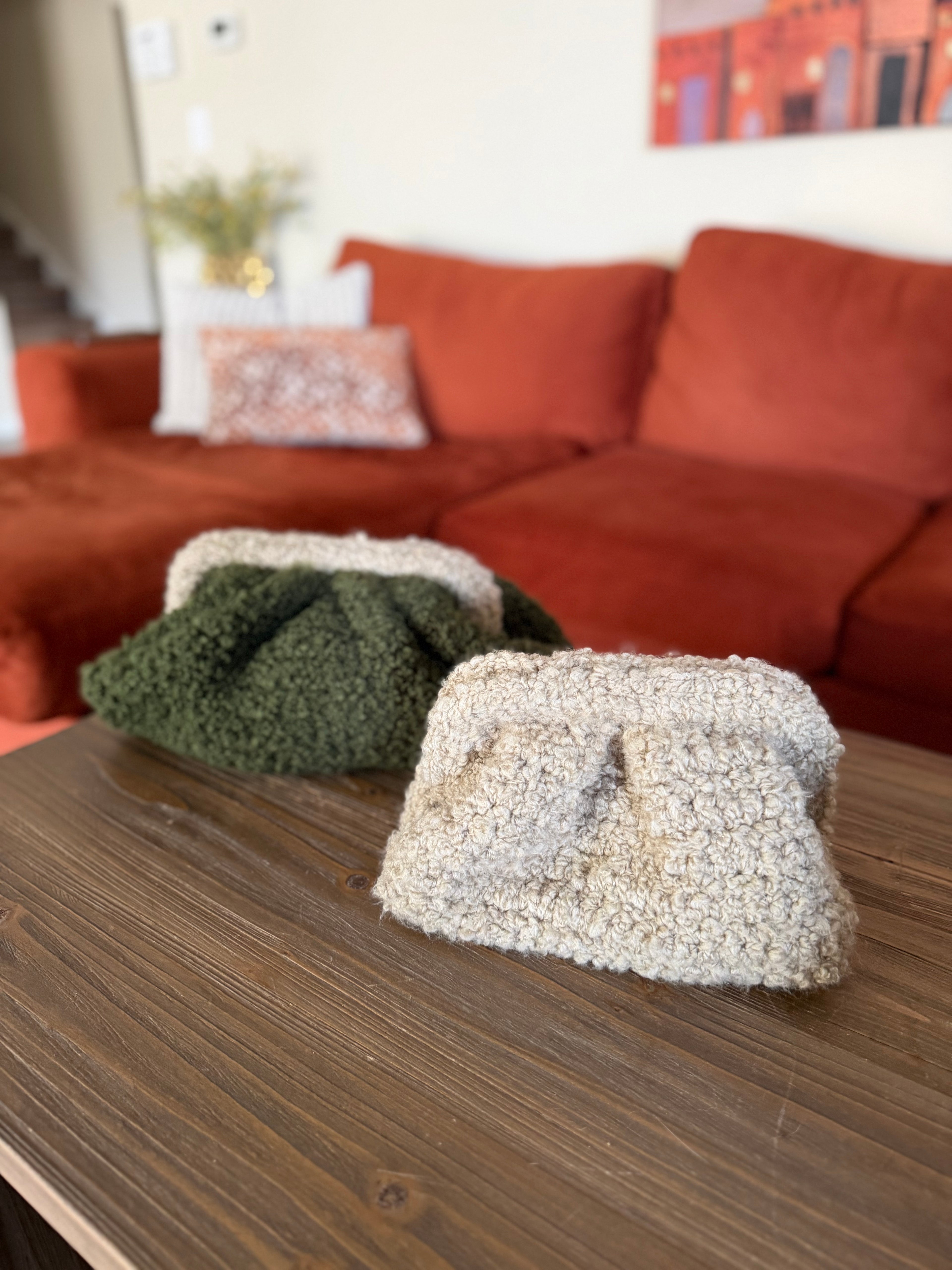 Two textured crochet clutches on a wooden table with a blurred orange sofa in the background