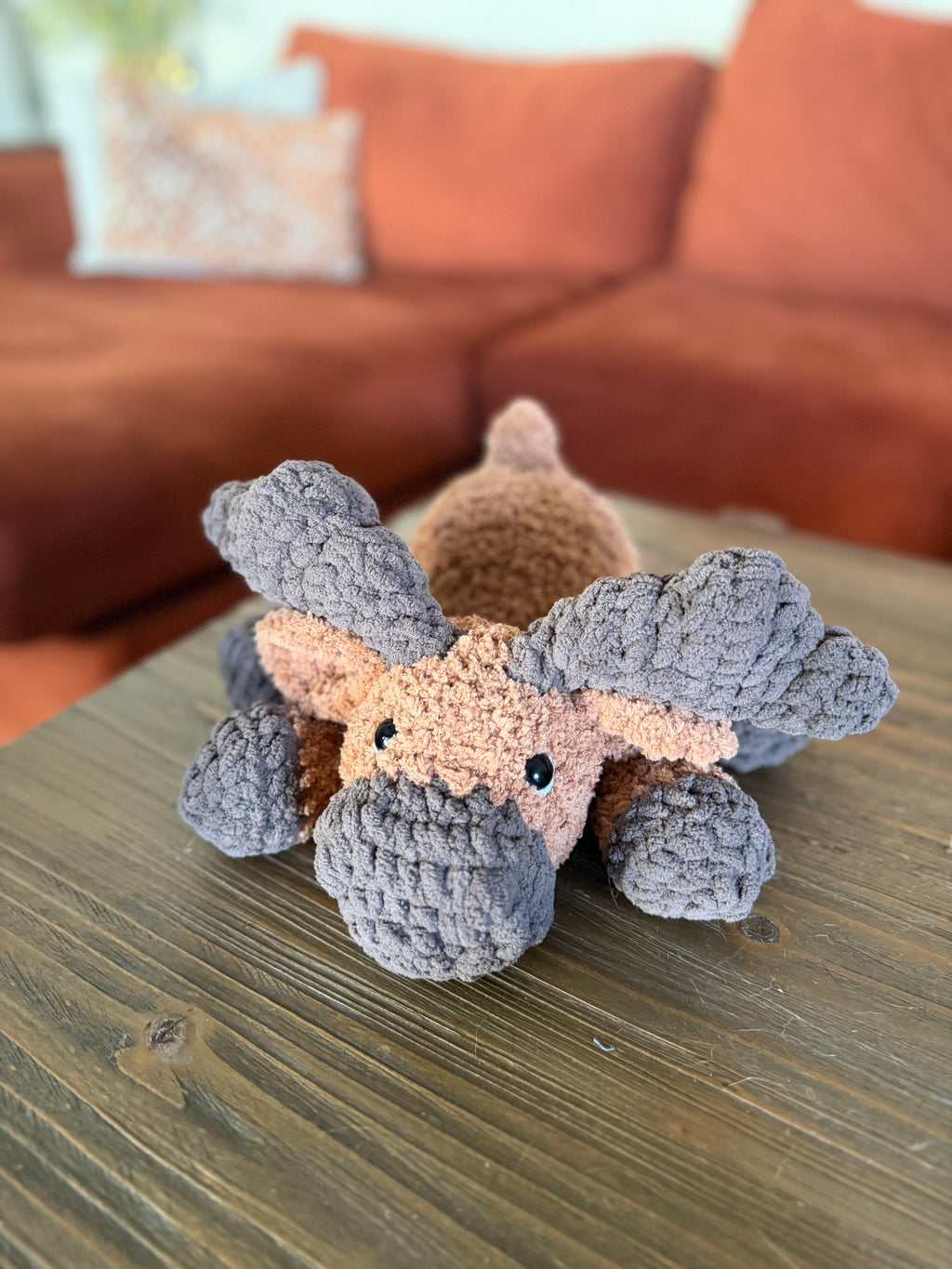 dark and light brown crochet moose in front of blurred orange couch