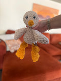 Hand holding a small beige and yellow crochet chicken plushie against a blurred orange couch