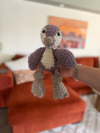 Purple and white penguin crochet plushie in front of blurred orange couch