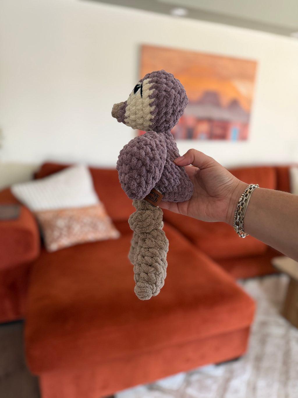 side profile of purple and white penguin crochet plushie in front of blurred orange couch