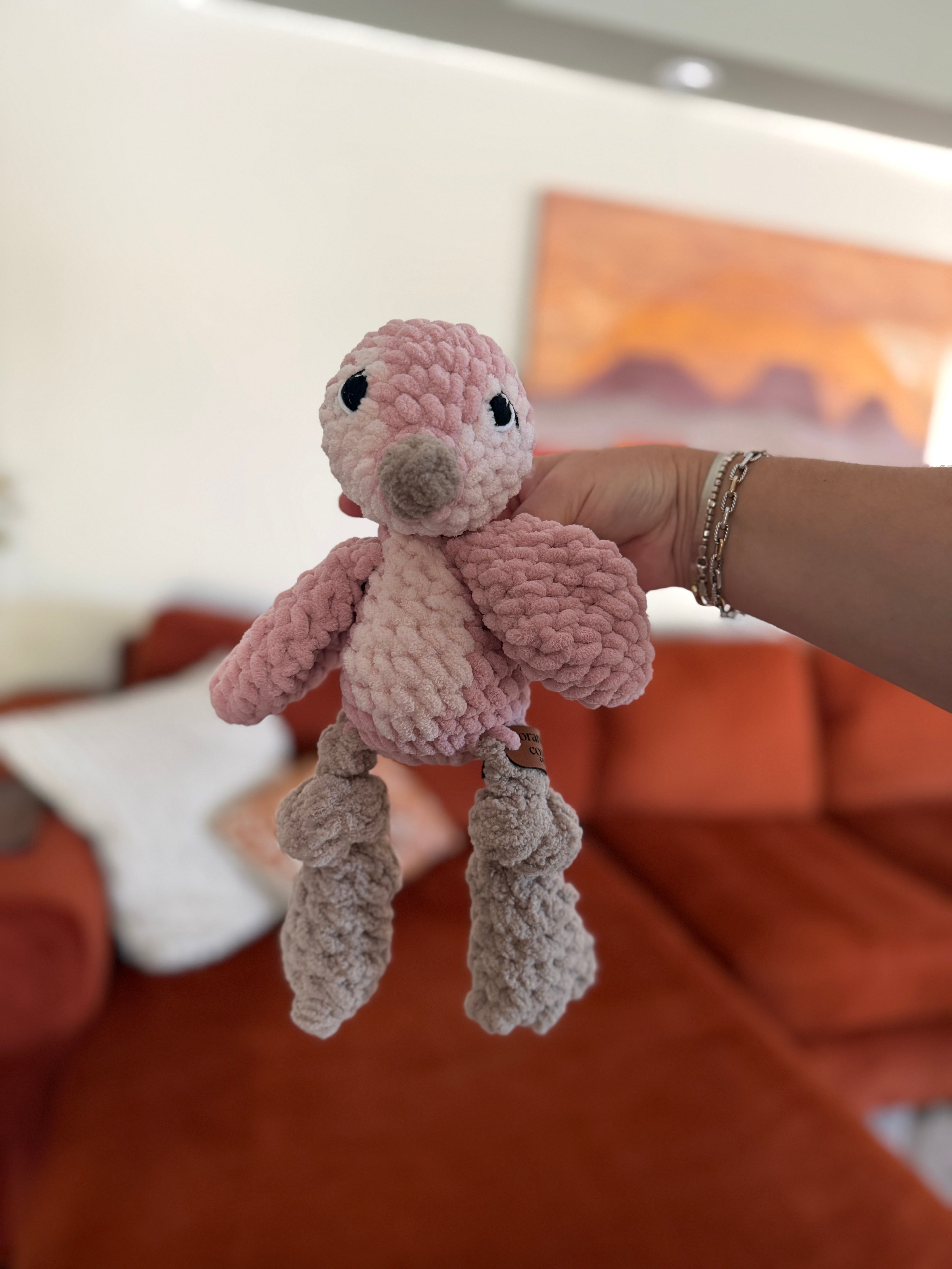 Pink and white penguin crochet plushie in front of blurred orange couch