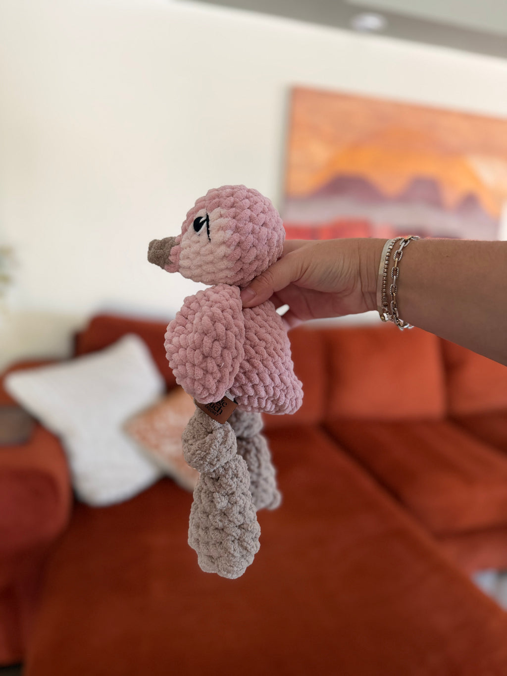 Side profile of pink and white penguin crochet plushie in front of blurred orange couch