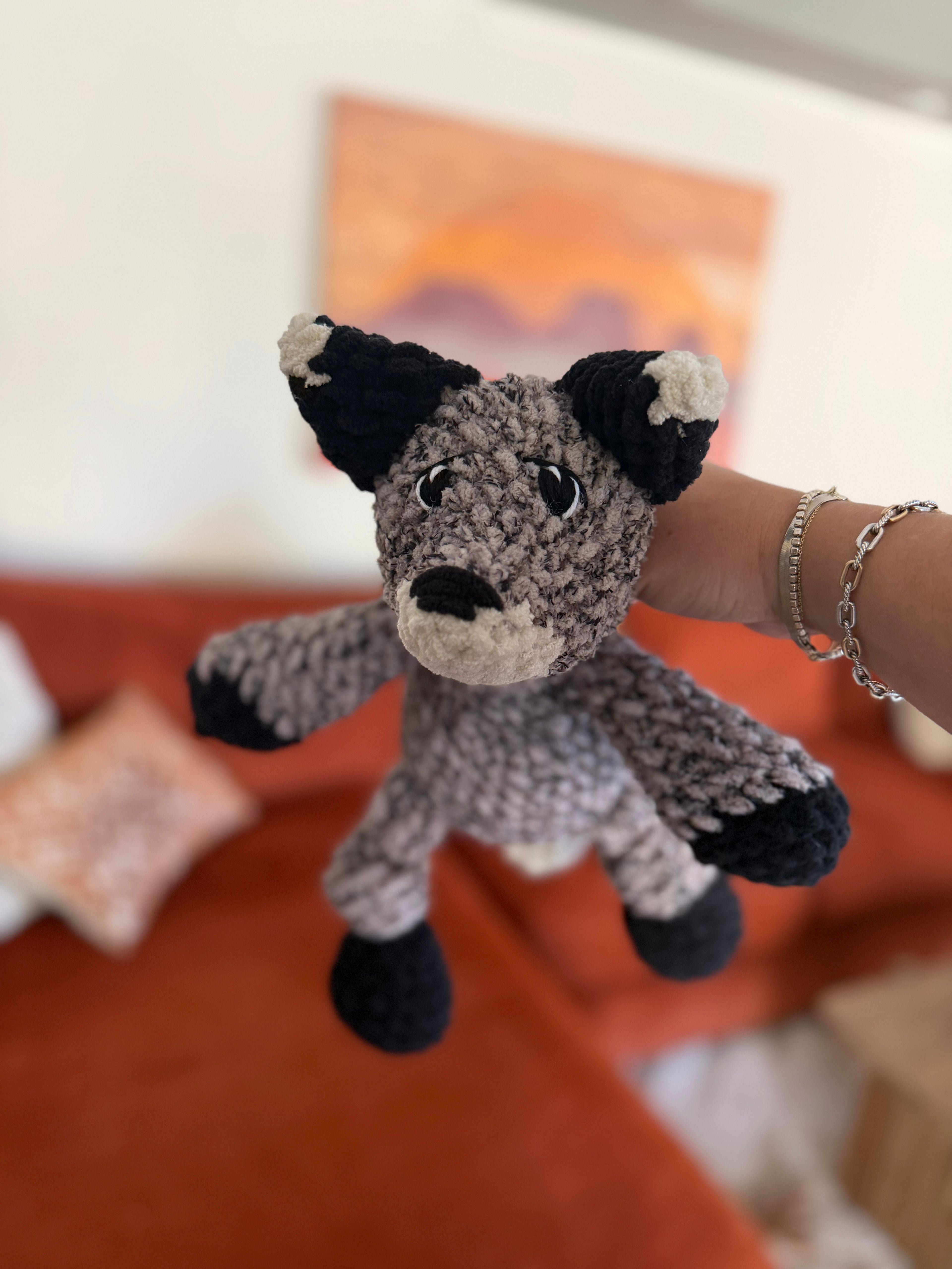 Black, white, and heathered grey crochet fox in front of blurred orange couch