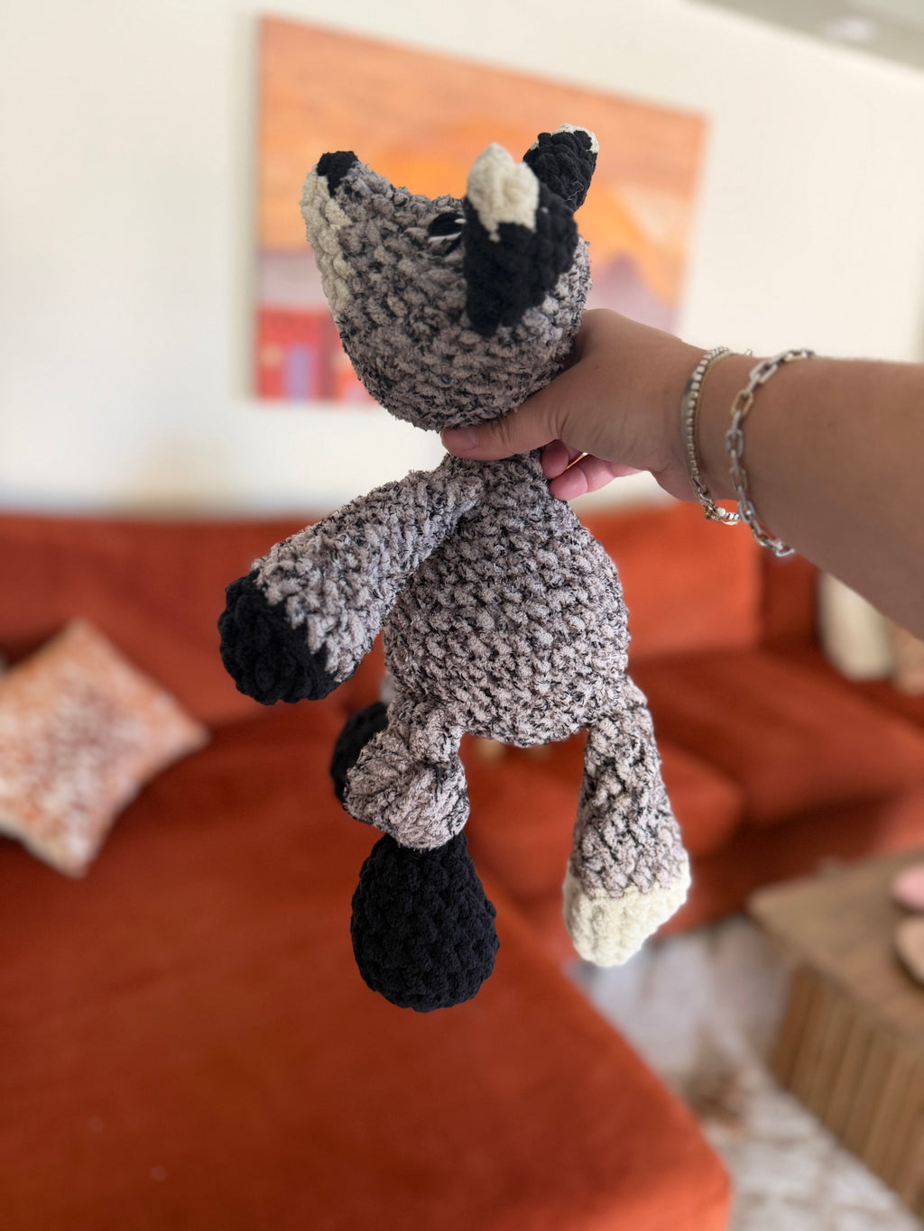 Side profile of black, white, and heathered grey crochet fox in front of blurred orange couch