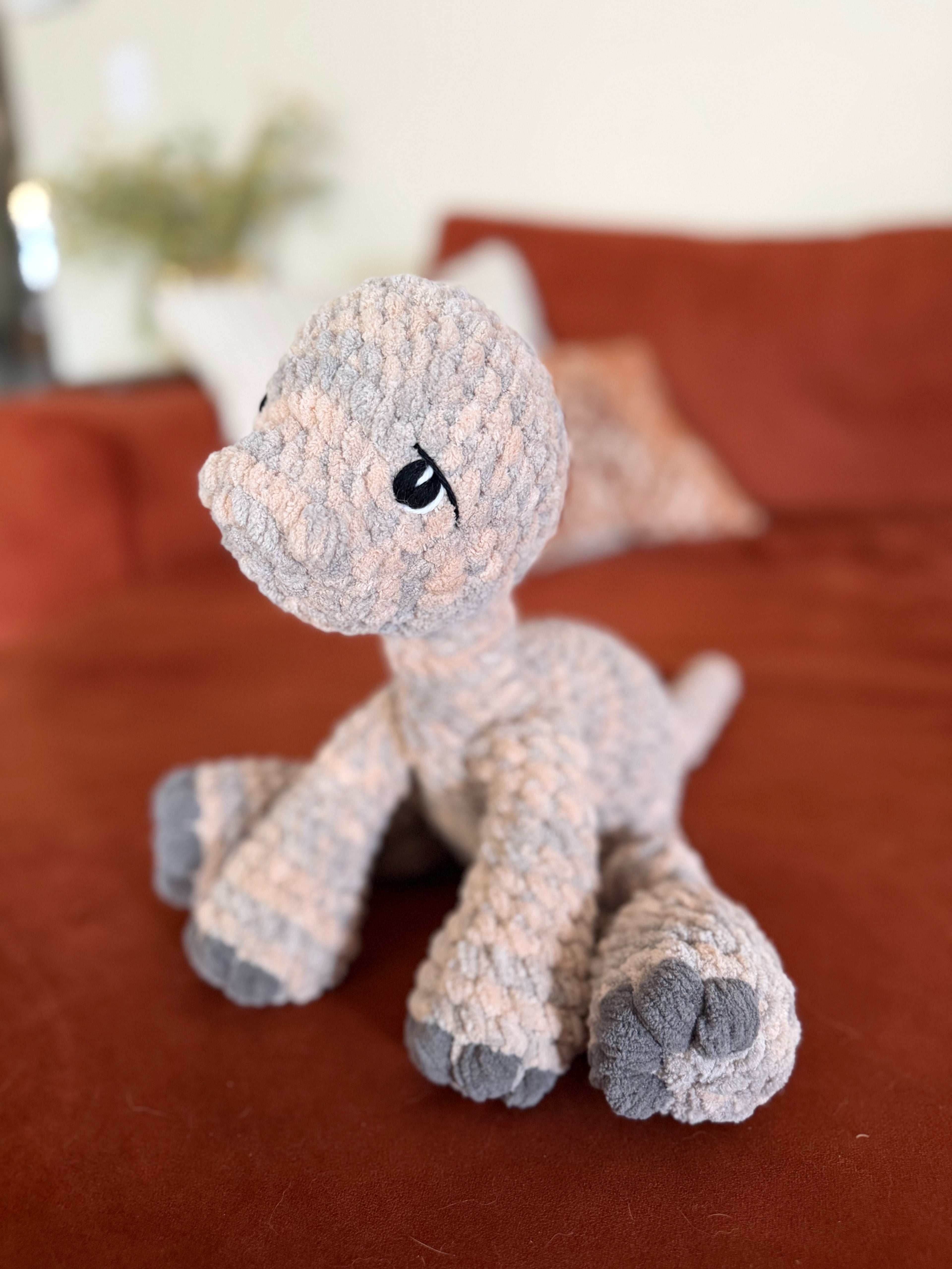 Longneck dino crochet plushie on an orange couch