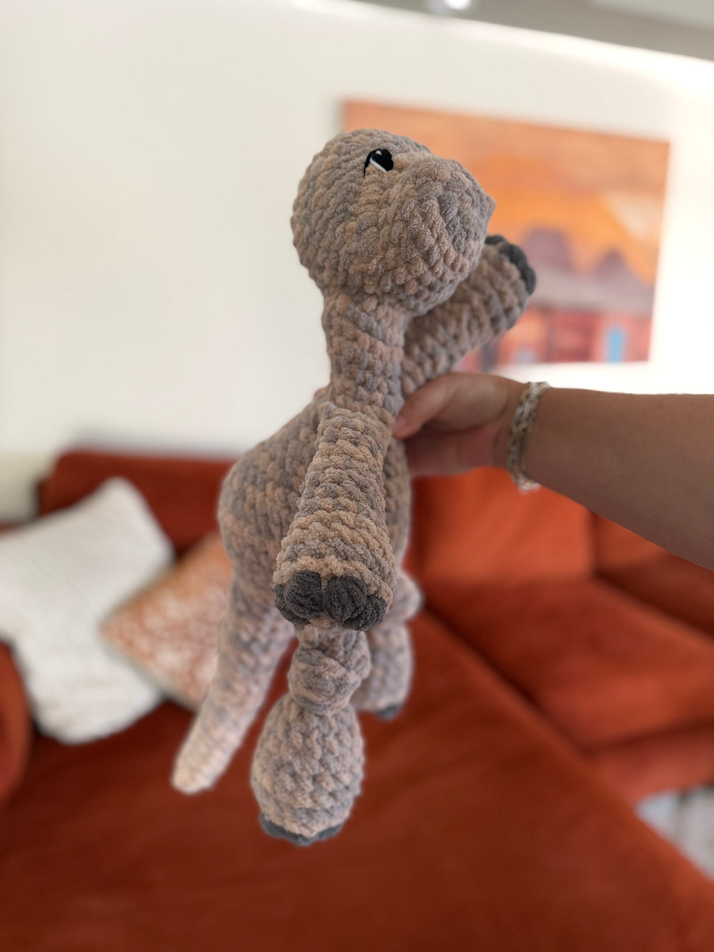Side profile of a skin-toned longneck Dino crochet plushie in front of blurred orange couch