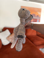 Side profile of a skin-toned longneck Dino crochet plushie in front of blurred orange couch