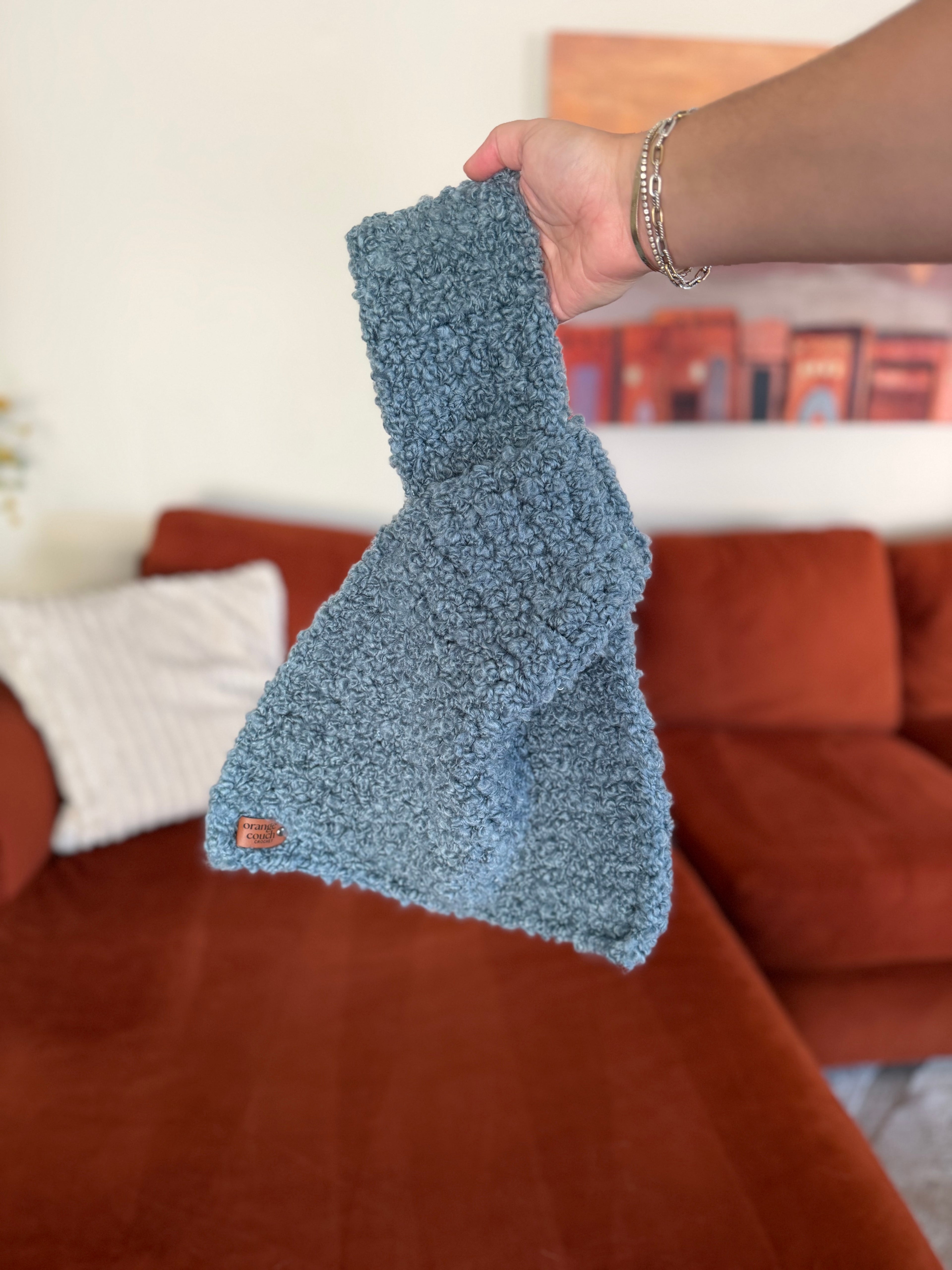 Crocheted blue Japanese knot bag in front of blurred orange couch